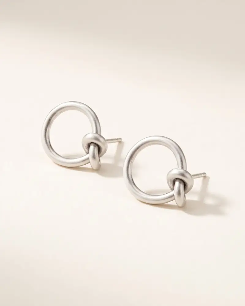 Karen-Silber-Ohrstecker „Knoten-Ring“ – Karen-Silber-Ohrstecker mit Knoten auf dunklem Grund