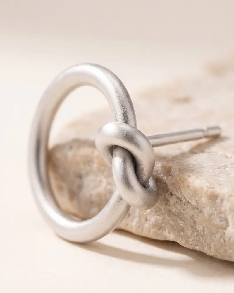 Karen-Silber-Ohrstecker „Knoten-Ring“ – Anwendung: Karen-Silber-Ohrstecker mit Knoten auf dunklem Grund